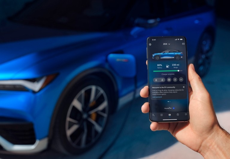 Acura ZDX 2024 Type S en Apex Blue Pearl cargando en segundo plano; en primer plano, un teléfono con la interfaz de la aplicación Acura EV