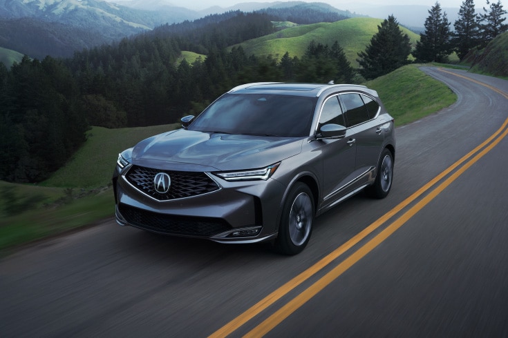 Vista de tres cuartos de la Acura MDX 2026 con Paquete Avanzado en Liquid Carbon Metallic conduciendo por una carretera (SUV de rendimiento prémium). Vista de tres cuartos de la Acura MDX 2026 con Paquete Avanzado en Liquid Carbon Metallic conduciendo por una carretera (SUV de rendimiento prémium).