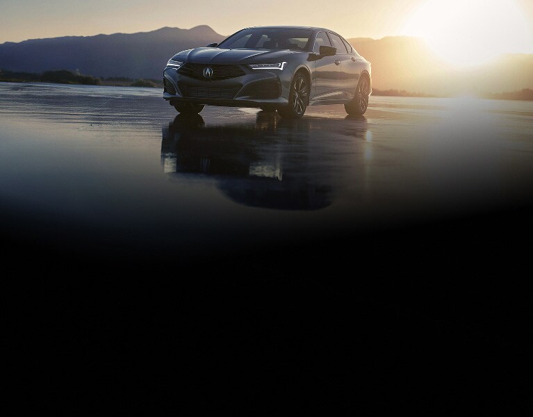 Vista frontal de 3/4 del Acura TLX 2026 con Paquete Tecnológico en Liquid Carbon Metallic al amanecer con montañas (sedán deportivo prémium).
