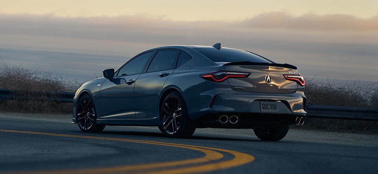 Vista trasera de la Acura TLX 2026 con Paquete Tecnológico en Liquid Carbon Metallic con una puesta de sol en el fondo (sedán deportivo prémium).